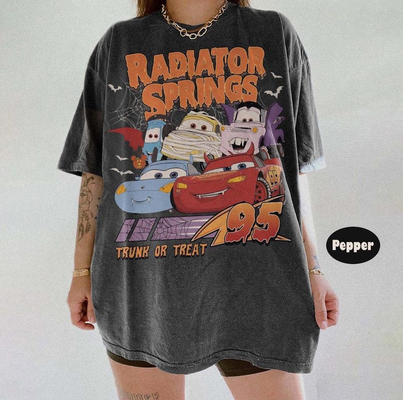 May include: Dark gray t-shirt featuring a graphic of characters from the movie Cars, with the text "Radiator Springs" in orange and "Trunk or Treat" below. The design includes bats and a spiderweb, with the number 95 in orange.