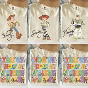 May include: A collection of cream-colored t-shirts featuring Toy Story characters. Three shirts display Woody, Jessie, or Buzz Lightyear with their names in script. Three shirts feature the colorful text You've Got A Friend In Me with characters.