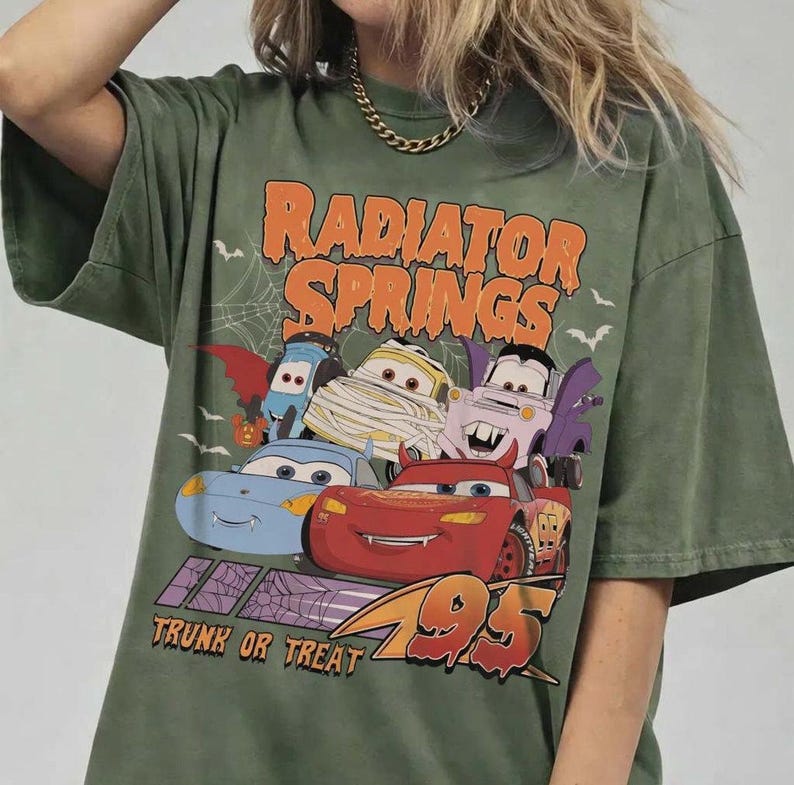 May include: Green t-shirt featuring a Halloween-themed graphic of the Cars characters. The design includes the text "Radiator Springs" and "Trunk or Treat 95". The graphic features Lightning McQueen and other characters in costumes.