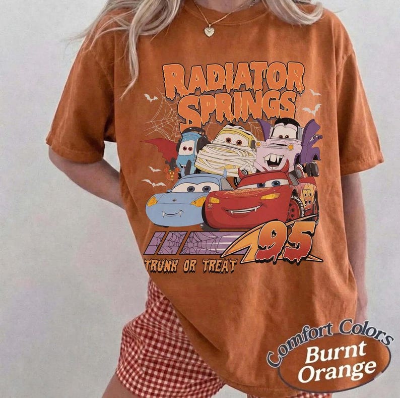 May include: Burnt orange t-shirt featuring a graphic of cartoon cars from Radiator Springs, with the text "Radiator Springs" and "Trunk or Treat". The shirt also has the text "Comfort Colors" and "Burnt Orange".