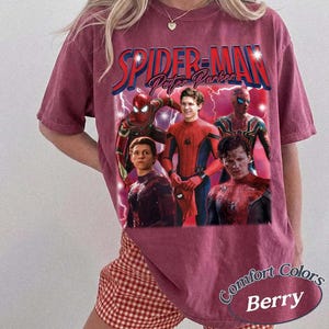 May include: Berry-colored t-shirt featuring a graphic of Spider-Man and Peter Parker. The design includes multiple images of the character, with the words "SPIDER-MAN" and "Peter Parker" in a vintage style. The shirt is labeled "Comfort Colors Berry".