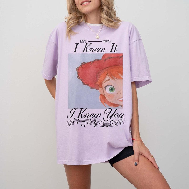 Peut inclure: Un t-shirt violet clair avec un motif repr&eacute;sentant un personnage de dessin anim&eacute; aux cheveux roux portant un chapeau rouge. Le texte indique EST 2026 I Knew It I Knew You, avec une port&eacute;e musicale. Le t-shirt a des manches courtes.
