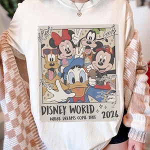 May include: Cream-colored sweatshirt featuring a Disney World graphic with Mickey Mouse, Minnie Mouse, Donald Duck, Goofy, and Pluto. The graphic includes the text "Disney World 2026" and signatures.