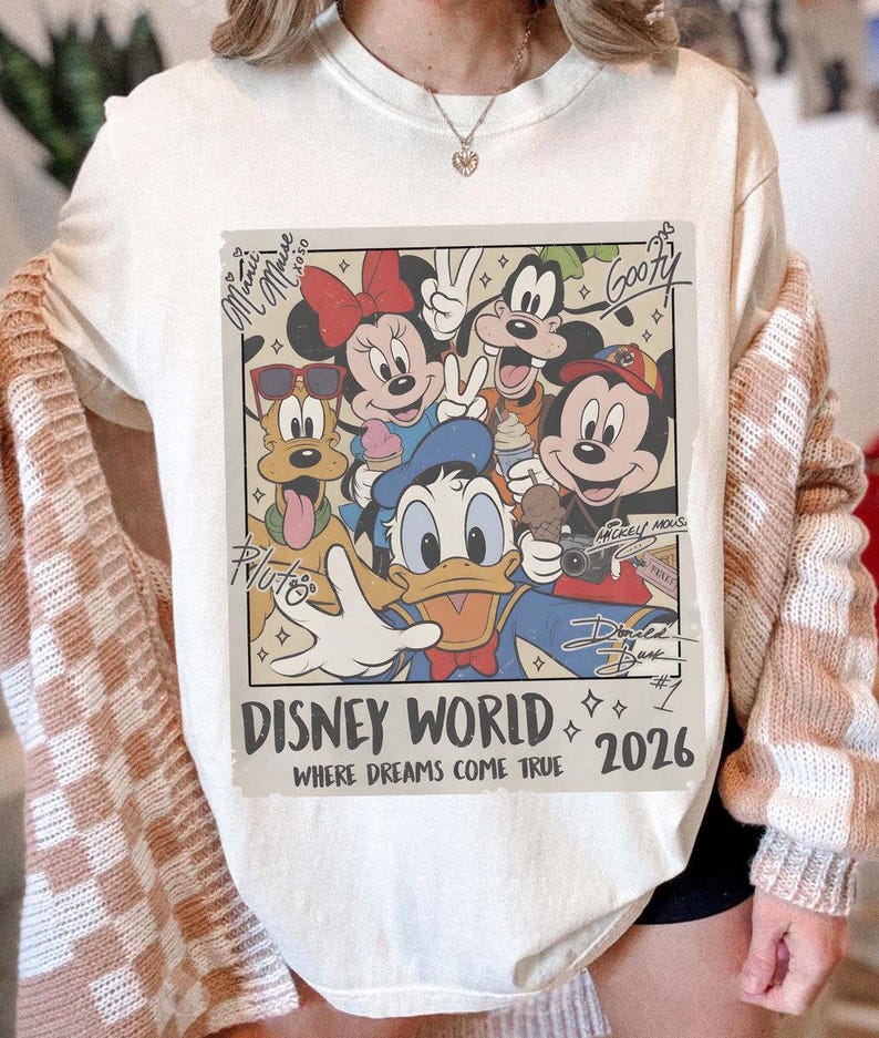 May include: Cream-colored sweatshirt featuring a Disney World graphic with Mickey Mouse, Minnie Mouse, Donald Duck, Goofy, and Pluto. The graphic includes the text "Disney World 2026" and signatures.