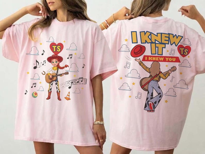 Puede incluir: Una camiseta rosa claro con un gr&aacute;fico de una vaquera tocando la guitarra en la parte delantera y una persona tocando la guitarra en la parte trasera. La espalda incluye el texto I KNEW IT I KNEW YOU y un coraz&oacute;n rojo con TS. Incluye nubes y notas.