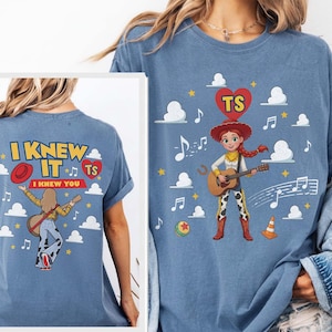 Puede incluir: Una camiseta azul con un gr&aacute;fico de una vaquera tocando la guitarra, rodeada de nubes, notas musicales y un coraz&oacute;n rojo con las letras TS. La parte posterior de la camiseta muestra el texto I KNEW IT I KNEW YOU con una ilustraci&oacute;n similar.
