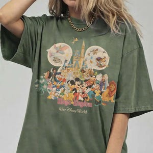 May include: Olive green t-shirt featuring a colorful graphic of Disney characters, including Mickey Mouse, Donald Duck, and Simba. The graphic also includes the text "Magic Kingdom Walt Disney World".