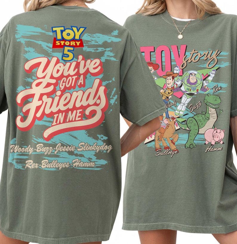 Pode incluir: Uma t-shirt verde-oliva com gr&aacute;ficos de Toy Story 5. As costas exibem o texto "You've Got A Friends In Me" com nomes de personagens. A frente mostra ilustra&ccedil;&otilde;es de Woody, Buzz Lightyear, Jessie, Bullseye, Rex e Hamm com o logo.