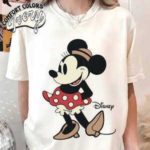 May include: A white ceramic mug with a black handle and the text "But First, Coffee" in a bold, black font. The mug is set against a blurred background, suggesting a cozy setting.