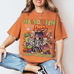 May include: Orange t-shirt with a Halloween-themed cartoon graphic. The text "HALLOWEEN STORY" is at the top, with "TO INFINITY AND BOO-YOND!" at the bottom. The design includes a ghost, dinosaur, and other characters, perfect for Halloween.