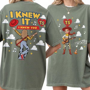 Puede incluir: Una camiseta verde oliva con un estampado gr&aacute;fico en la parte delantera y trasera. La parte trasera muestra un personaje con una guitarra, el texto I KNEW IT I KNEW YOU y un coraz&oacute;n rojo con TS. La parte delantera muestra el mismo personaje con una guitarra y un coraz&oacute;n rojo con TS.