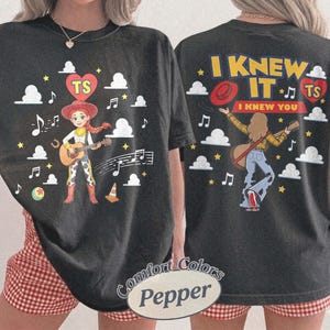 Puede incluir: Una camiseta negra con un gr&aacute;fico frontal de una vaquera tocando la guitarra con notas musicales, nubes y un coraz&oacute;n con las letras TS. El gr&aacute;fico trasero muestra a una persona tocando la guitarra con el texto I KNEW IT I KNEW YOU y un coraz&oacute;n.