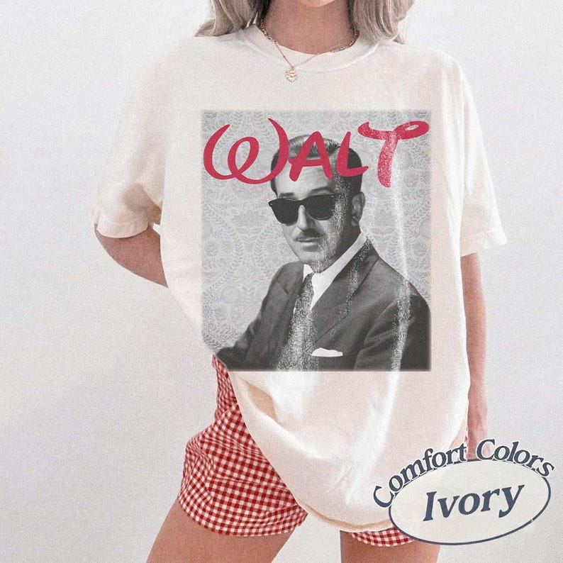 May include: Ivory-colored t-shirt featuring a black and white image of a man wearing sunglasses, with the word "WALT" in red script above. The shirt is a Comfort Colors brand.