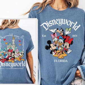 May include: A blue t-shirt featuring Disney characters. The front of the shirt displays the word "Disneyworld" above a group of cartoon characters. The back of the shirt has a castle graphic and the word "Disneyworld".