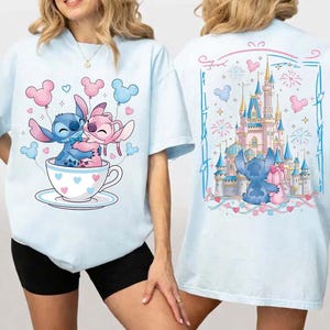 Pu&ograve; includere: T-shirt azzurra con un cartone animato di Stitch e Angel in una tazza, circondati da palloncini. Il retro della maglietta mostra un castello, Stitch e Angel con dei regali, in una cornice decorativa.
