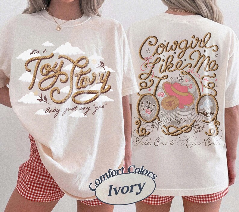 May include: An ivory t-shirt featuring a front graphic with rope-style text reading 'it's a Toy Story' and 'Baby, just say yes' amidst clouds. The back graphic displays 'Cowgirl like Me' and 'Takes One to Know One' with rope, a pink hat, and stars.