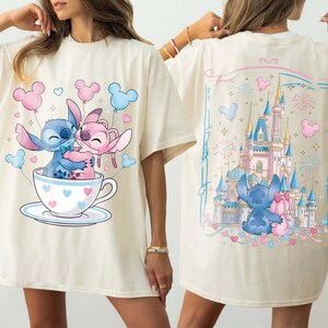 Pu&ograve; includere: T-shirt color crema con un'illustrazione a cartoni animati di Stitch e Angel in una tazza da t&egrave; con dettagli a cuore e palloncini di Topolino. Il retro della maglietta mostra una scena del castello con Stitch e Angel.
