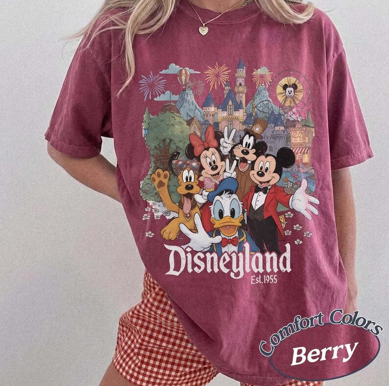 Pu&ograve; includere: Una t-shirt a maniche corte color bacca con una stampa grafica di Topolino, Minnie, Paperino, Pippo e Pluto davanti a un castello. Il testo "Disneyland Est. 1955" &egrave; stampato sotto i personaggi in un carattere serif di colore bianco.
