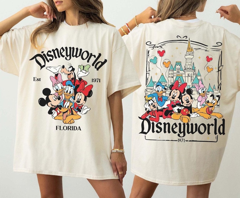 May include: Cream-colored t-shirt featuring the text "Disneyworld" with a graphic of Disney characters. The front of the shirt displays Mickey, Minnie, Donald, Daisy, Goofy, and Pluto. The back shows the Disney castle and more characters.