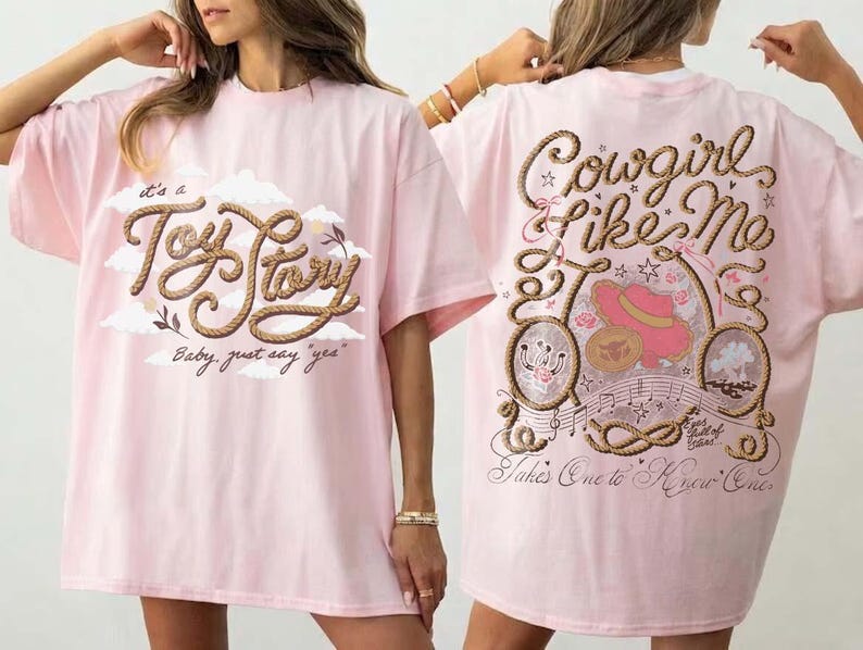 May include: A light pink t-shirt featuring a front graphic with the text "It's a Toy Story" in rope-style lettering and clouds. The back graphic displays the text "Cowgirl Like Me" and "Takes One to Know One" with rope borders, a pink hat, and musical notes.