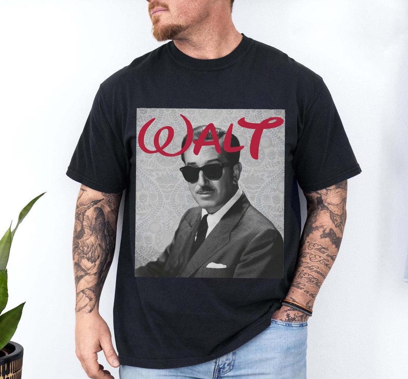 May include: Black t-shirt featuring a black and white image of a man wearing sunglasses and a suit. The word "WALT" is written in red cursive above the image. The shirt is a classic crew neck.