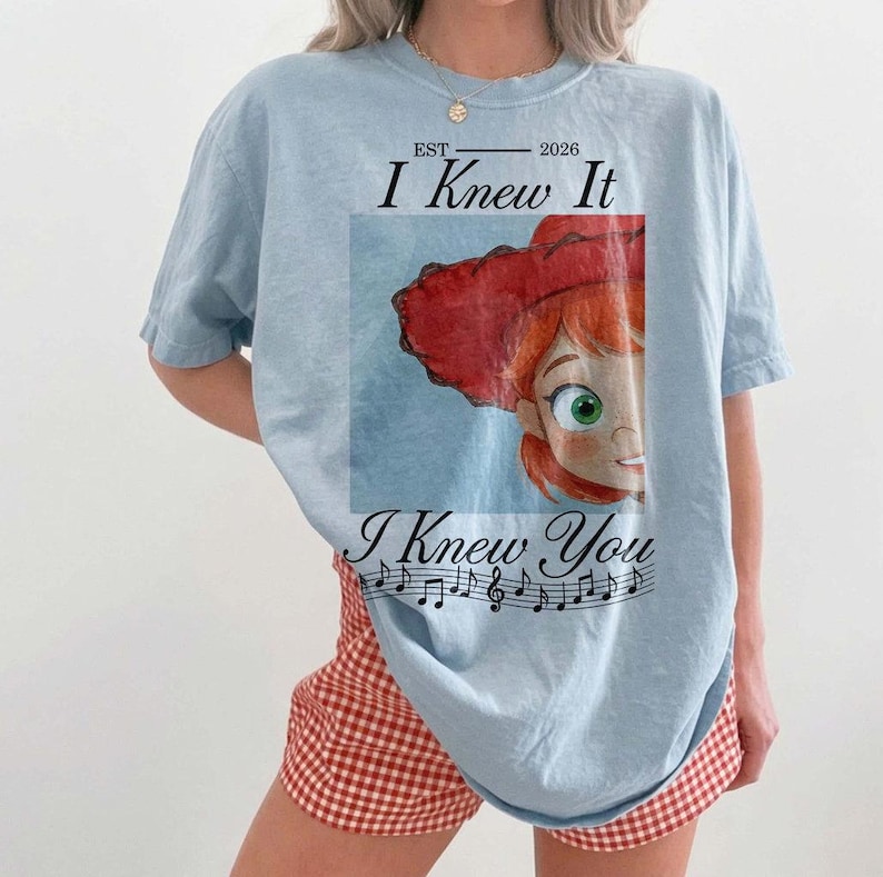 Peut inclure: Un t-shirt bleu clair avec une impression graphique repr&eacute;sentant un personnage de dessin anim&eacute; aux cheveux roux portant un chapeau rouge. Le texte "EST 2026 I Knew It I Knew You" est imprim&eacute; avec une port&eacute;e musicale et des notes noires.
