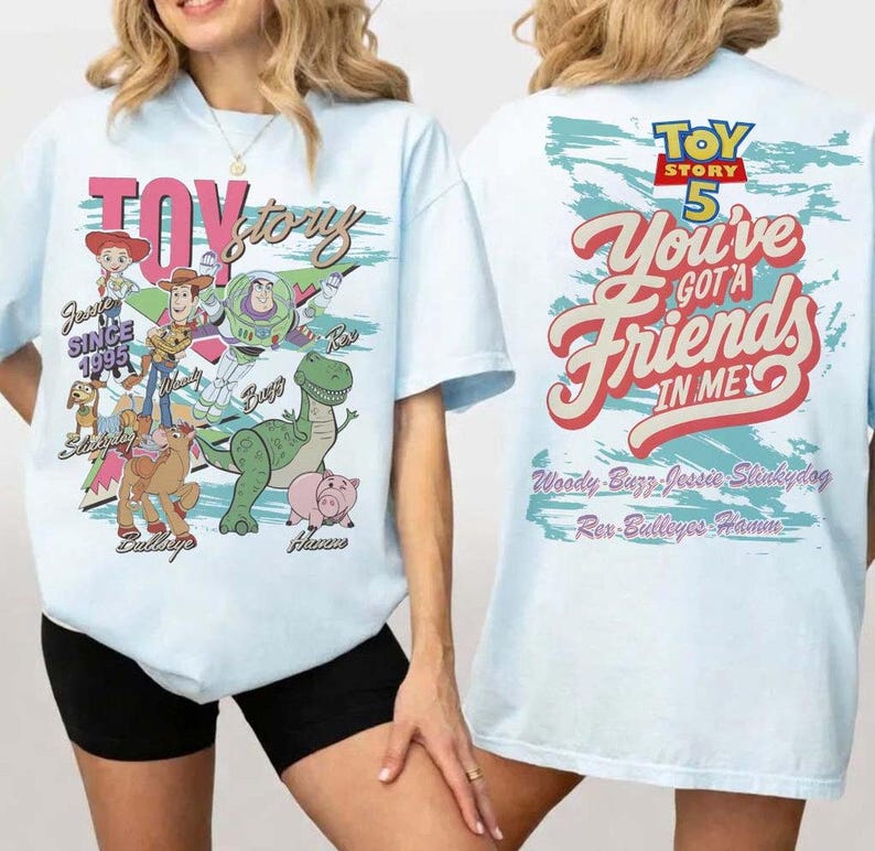 Pode incluir: Uma t-shirt azul-clara com gr&aacute;ficos de Toy Story. A frente exibe Woody, Buzz Lightyear, Jessie, Slinky Dog, Bullseye e Hamm com o texto "Toy Story SINCE 1995". As costas apresentam o texto "TOY STORY 5 You've Got A Friends In Me".