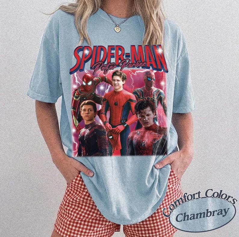 May include: Light blue t-shirt featuring a graphic of Spider-Man and the text "Spider-Man Peter Parker" in red and blue. The shirt has a vintage style and is made of a soft material. The bottom right corner of the shirt has the text "Comfort Colors Chambray".