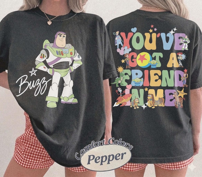 May include: A black t-shirt featuring a graphic of Buzz Lightyear and the text Buzz on the front. The back displays various Toy Story characters and the colorful text You've Got A Friend In Me. The shirt is labeled as Comfort Colors Pepper.