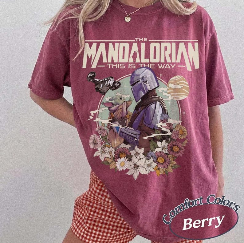 May include: Berry-colored t-shirt featuring a graphic from "The Mandalorian." The design includes the show's title, a depiction of the Mandalorian and Grogu surrounded by flowers, and the text "This is the Way."