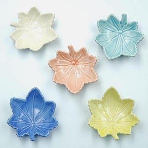 Op de afbeelding: Vijf keramische bladschalen in pastelkleuren: crème, lichtblauw, roze, blauw en geel. Elke schaal heeft een gedetailleerd bladnerfdesign en een kleine steel. Deze decoratieve schalen zijn ideaal voor het serveren van kleine porties.