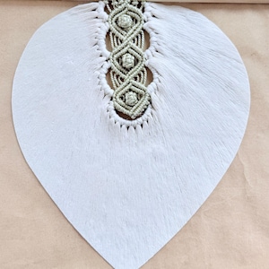 Pode incluir: Um pendurador de parede artesanal com um design grande em forma de folha cinza claro. O centro tem um padr&atilde;o de macram&eacute; em uma cor verde suave, com um pino de madeira na parte superior para pendurar. A textura da folha &eacute; vis&iacute;vel.