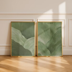 Può includere: Due stampe artistiche rettangolari verticali incorniciate in sottile metallo dorato. Ogni stampa presenta colline astratte a strati in varie tonalità di verde salvia e bosco, caratterizzate da visibili texture a pennellate sulla superficie.