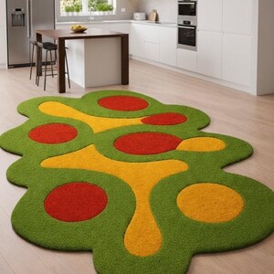 May include: A colorful, abstract rug with a green, yellow, and red design. The rug features a unique, organic shape with circular and flowing patterns. The rug is placed on a light-colored wooden floor in a modern kitchen setting.