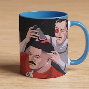 May include: A ceramic coffee mug with a blue interior and handle, featuring a cartoon illustration. The artwork depicts two men, one in a red shirt, the other in a white suit, with a futuristic theme. The mug sits on a wooden surface.
