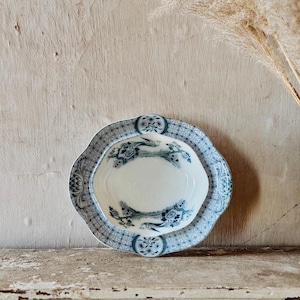 May include: Two-piece vintage serving dish set. The set includes a large, scalloped-edge plate and a smaller, oval-shaped dish. Both pieces feature a white background with blue floral and bird designs, and a geometric border.
