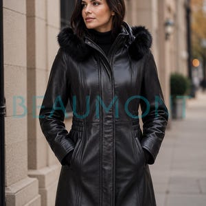 Può includere: Un cappotto in pelle nera con cappuccio bordato in pelliccia sintetica nera, collo alto e chiusura frontale con zip nascosta da una patta. Il cappotto presenta maniche lunghe, tasche laterali e un dettaglio in vita. La scritta BEAUMONT è visibile.