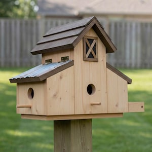 May include: A wooden birdhouse with a brown shingled roof and a small window with an X design. The birdhouse has two circular entry holes and a small perch. It is mounted on a wooden post and set against a blurred green background.