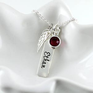 May include: Silver necklace with a small red gemstone, a silver angel wing charm, and a silver bar charm engraved with the name "Ethan".