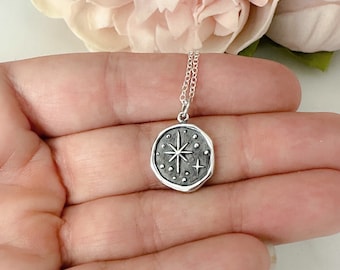 May include: A silver necklace with a charm featuring a star with a textured surface and small dots around it.