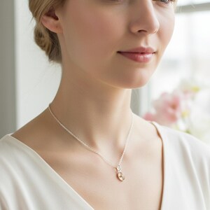May include: A silver necklace with a small, round pendant. The pendant has a gold-colored center and a silver-colored outer ring. The necklace is worn by a person wearing a white top.