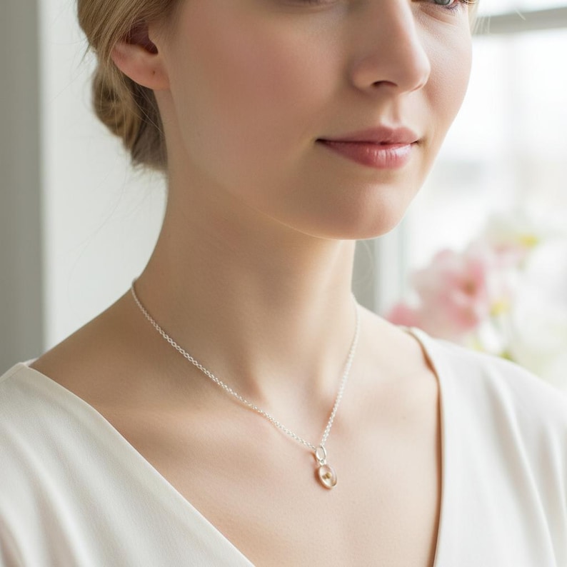 May include: A silver necklace with a small, round pendant. The pendant has a gold-colored center and a silver-colored outer ring. The necklace is worn by a person wearing a white top.