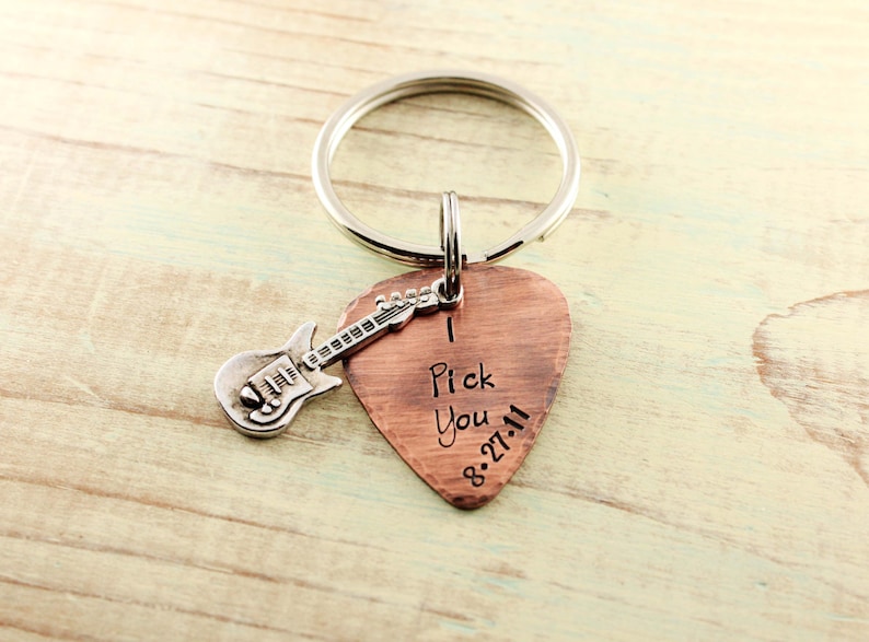 May include: A copper guitar pick keychain with a silver guitar charm. The pick has the words "I Pick You 8.27.11" engraved on it.