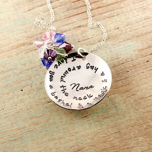 May include: Silver necklace with a round pendant that reads "I love you more than a bushel of  peonies,  but I  only  buy  you  a  bushel  of  peonies  for  my  Nana  neck  &  a  peck  of  peonies  for  the  rest". The pendant is adorned with a cluster of colorful crystals.