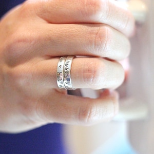 May include: Two silver rings with the names "Eva" and "Michael" engraved on them. The rings are worn on a finger.