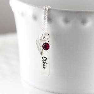 May include: Silver necklace with a small red gemstone, a charm with angel wings, and a personalized tag that reads "Ethan".