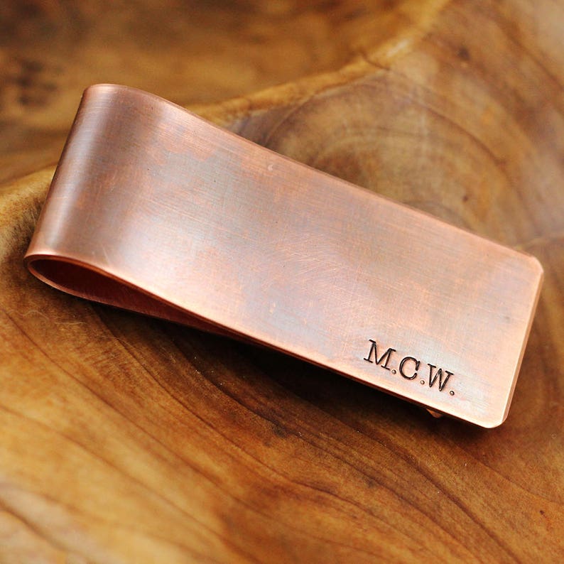 May include: A copper money clip with a brushed finish and the initials "M.C.W." engraved on the front.