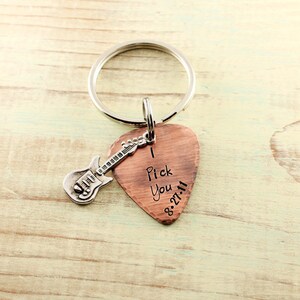May include: Copper guitar pick keychain with a silver guitar charm. The pick has the words "I Pick You" and the date "8-27-11" engraved on it.