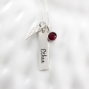 May include: Silver necklace with a small wing charm, a red gemstone, and a rectangular tag engraved with the name "Ethan".