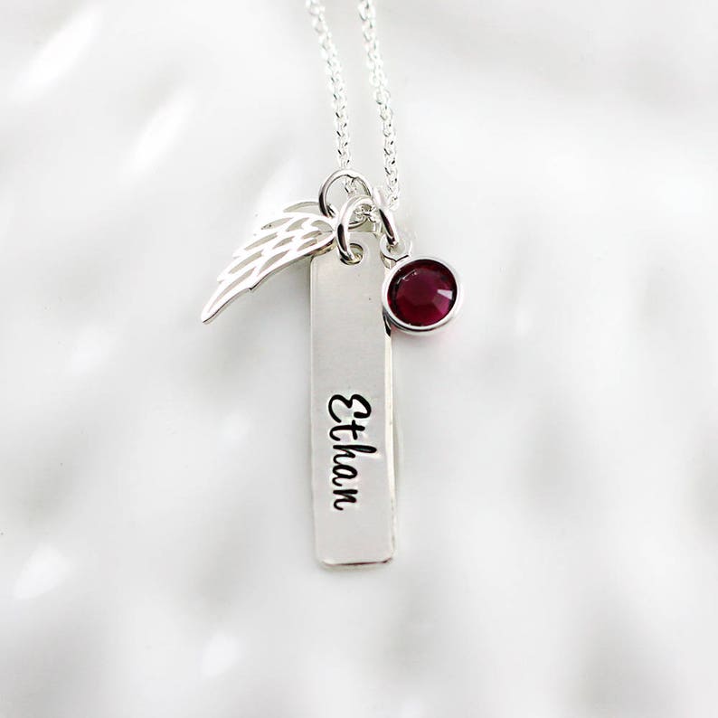 May include: Silver necklace with a small wing charm, a red gemstone, and a rectangular tag engraved with the name "Ethan".
